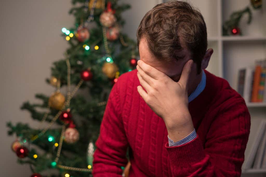 A man with his head in his hands, sitting near a Christmas tree.