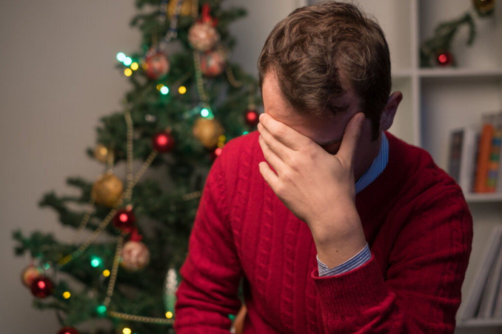 En mann med hodet i hendene, sittende nær et juletre.