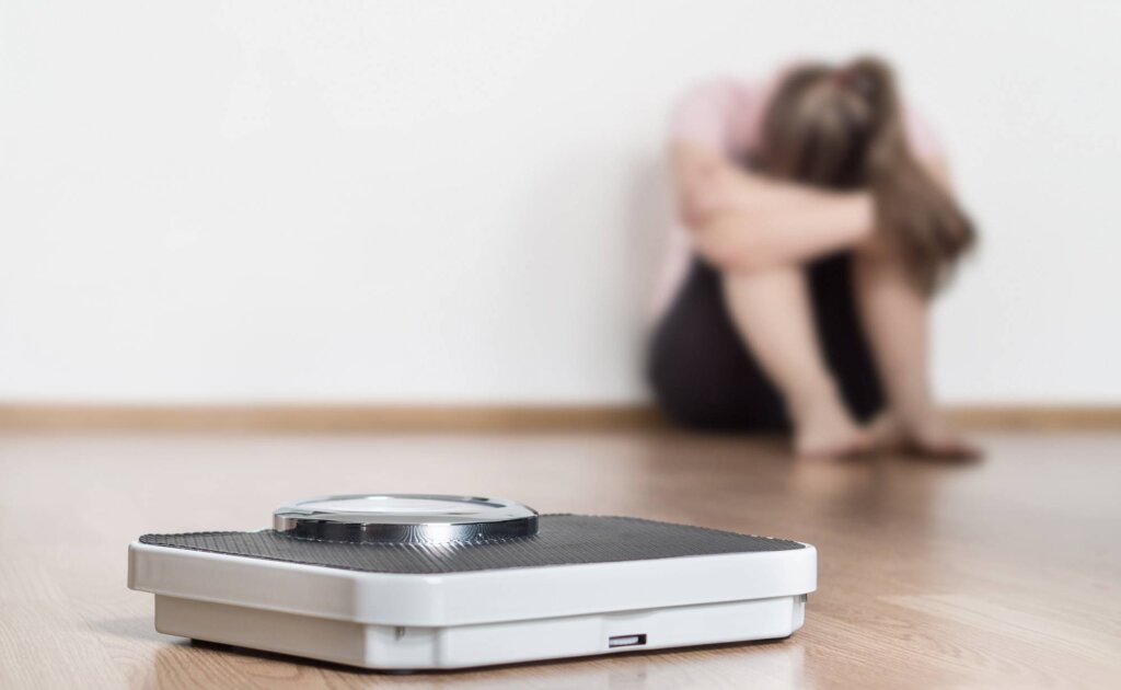 chica ante báscula simbolizando el vinculo entre la Obesidad y trastornos de la conducta alimentaria