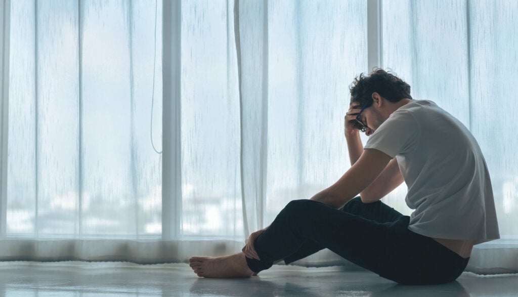 Worried man sitting on the floor next to a large window with white curtains