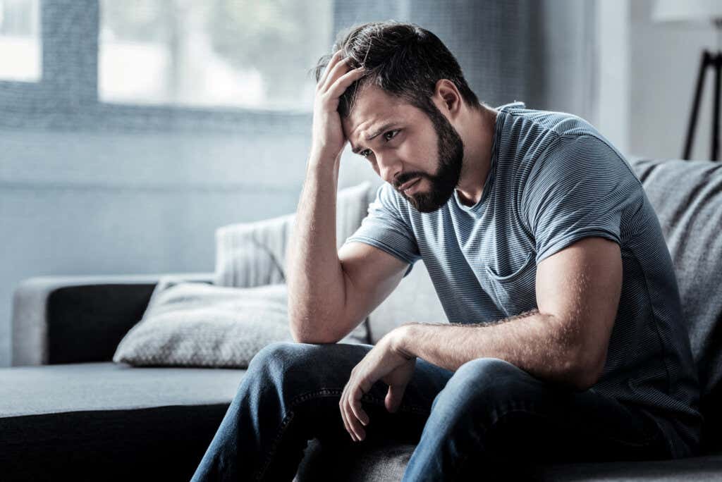 Bekymret mann som sitter i stuen i et hus og lider av emosjonelt sjokk
