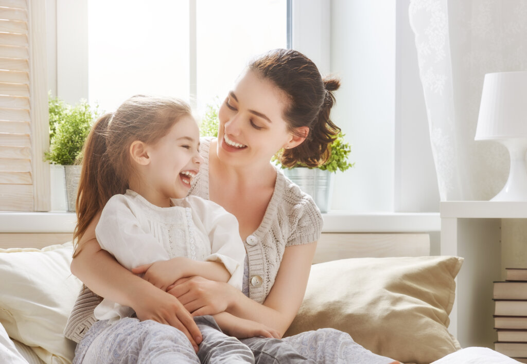 Mãe e filha sorriem sentadas em um sofá