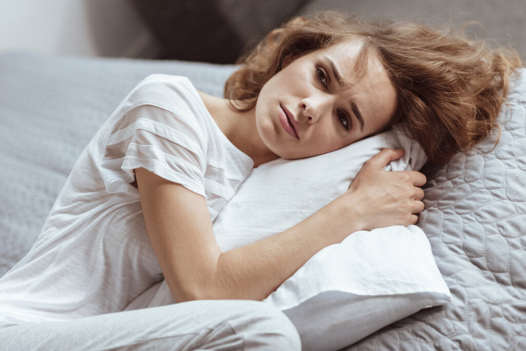 Mulher vestida de branco deitada em sua cama abraça um travesseiro