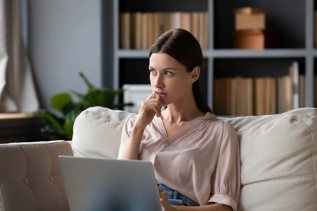 Kvinne som sitter på en sofa foran datamaskinen og tviler på grunn av manipulatorene
