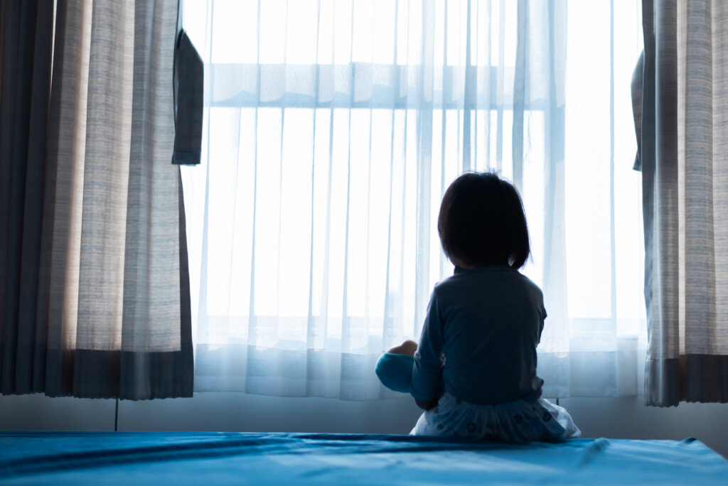 Fille seule dans une pièce regardant par la fenêtre