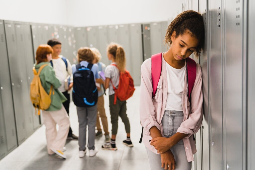 As crianças ignoram a menina que se senta sozinha no corredor da escola