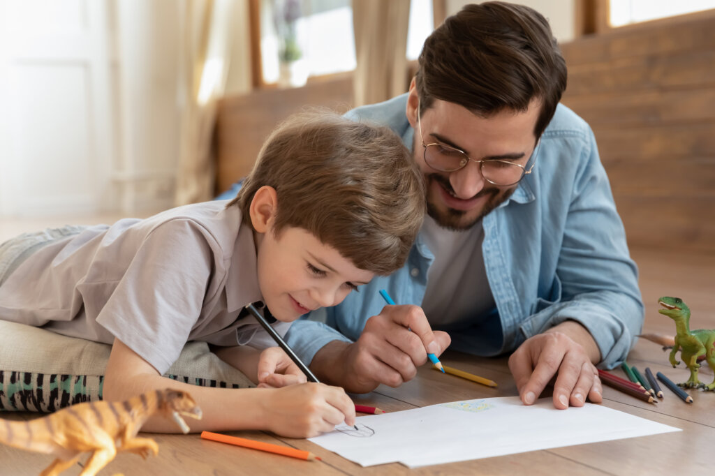 Père et fils dessinant sur le sol avec un dinosaure jouet de côté