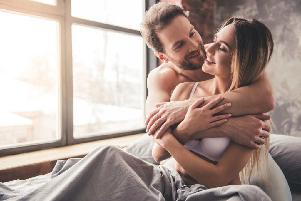 Couple câlins au lit à côté d'une fenêtre