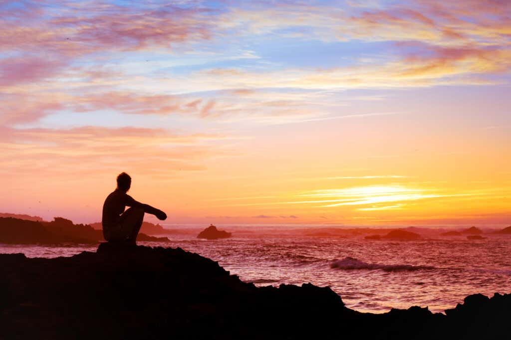 Kvinne som sitter og betrakter solnedgangen og reflekterer over meningen med livet