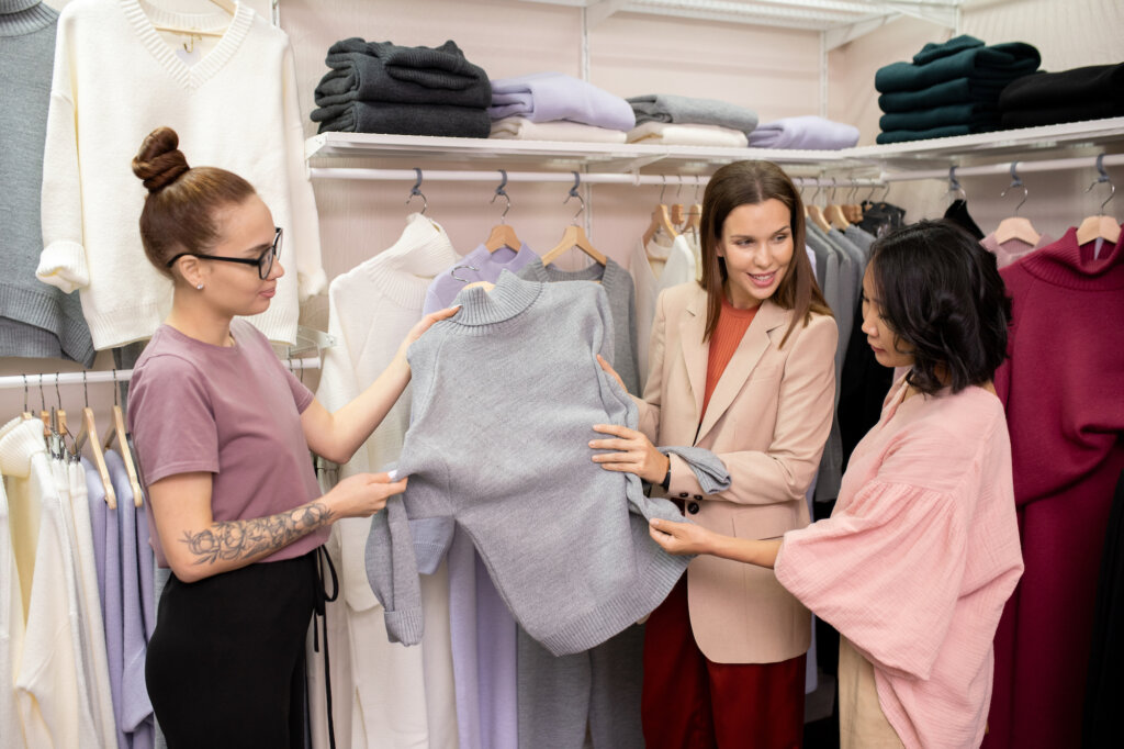 Duas vendedoras mostram uma peça de roupa para um cliente que demonstra empatia