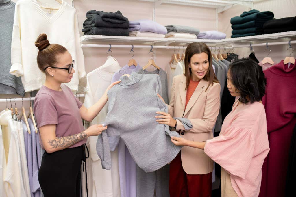 Dwie sprzedawczynie pokazują ubranie klientowi, który okazuje empatię