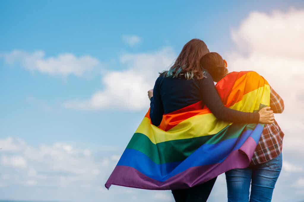 Pareja lesbiana abrazada con la bandera de la comunidad LGTB