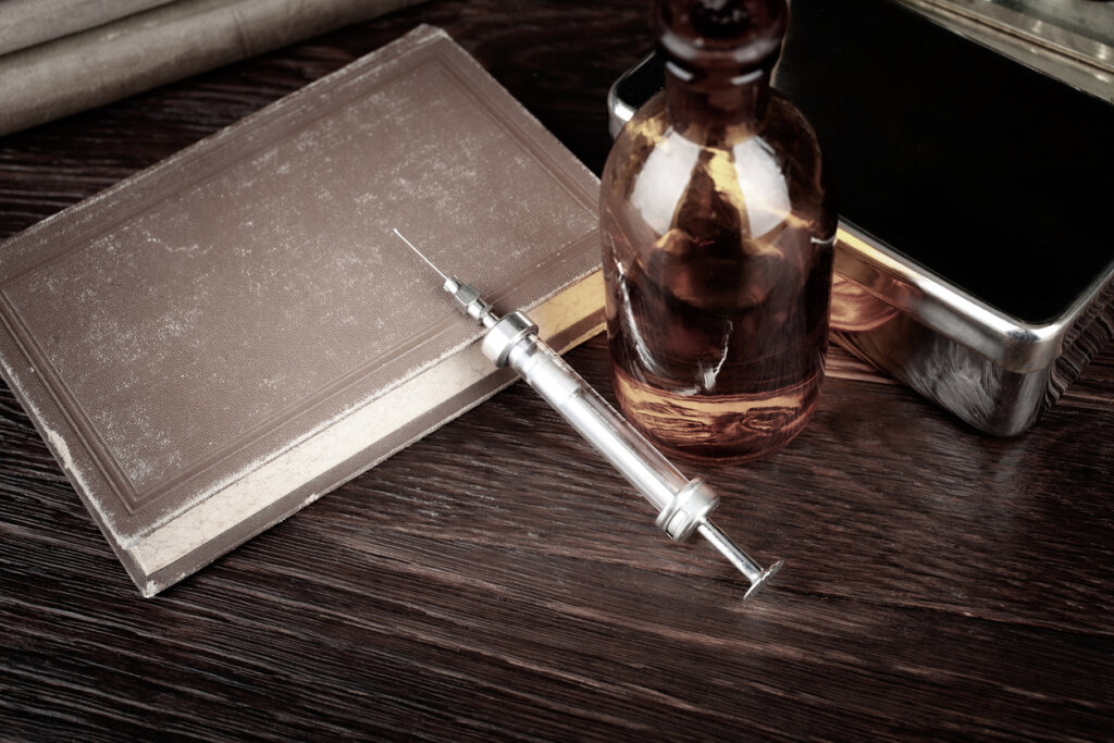 Syringe and vial of morphine on a wooden table alluding to the addictions of the writer Friedrich Glauser