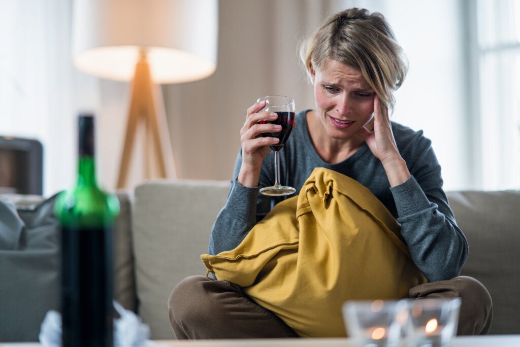 Une femme assise sur un canapé avec une crise d'anxiété boit un verre de vin