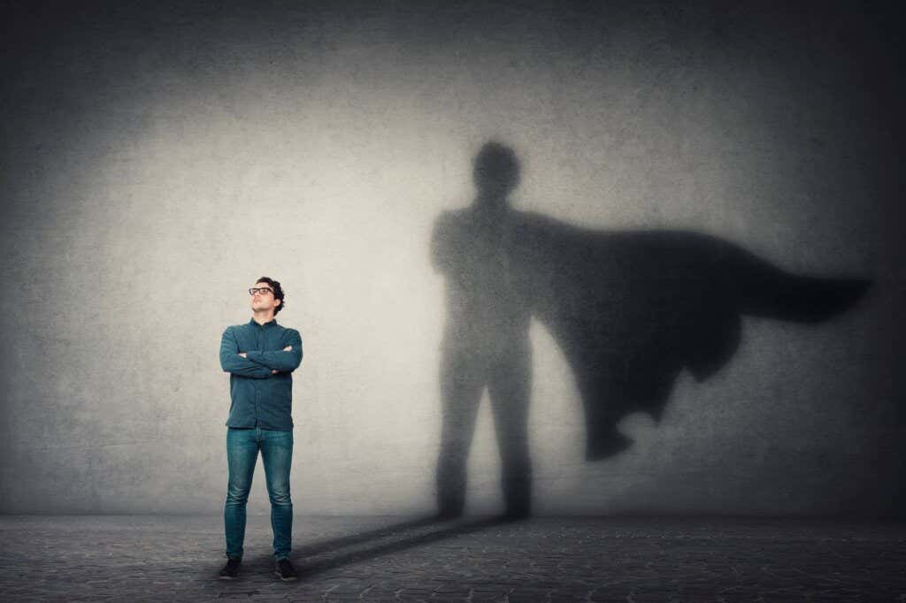 Person standing with arms crossed and behind is a shadow of the person with a cape that alludes to power
