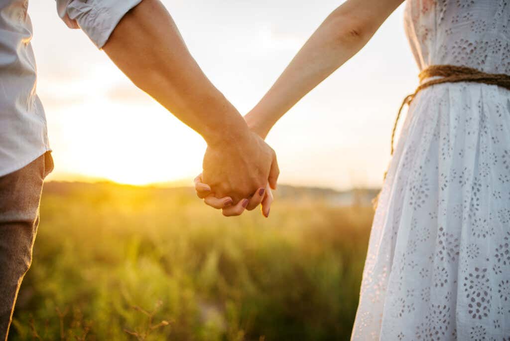 A couple holding hands while watching the sunset over a field.