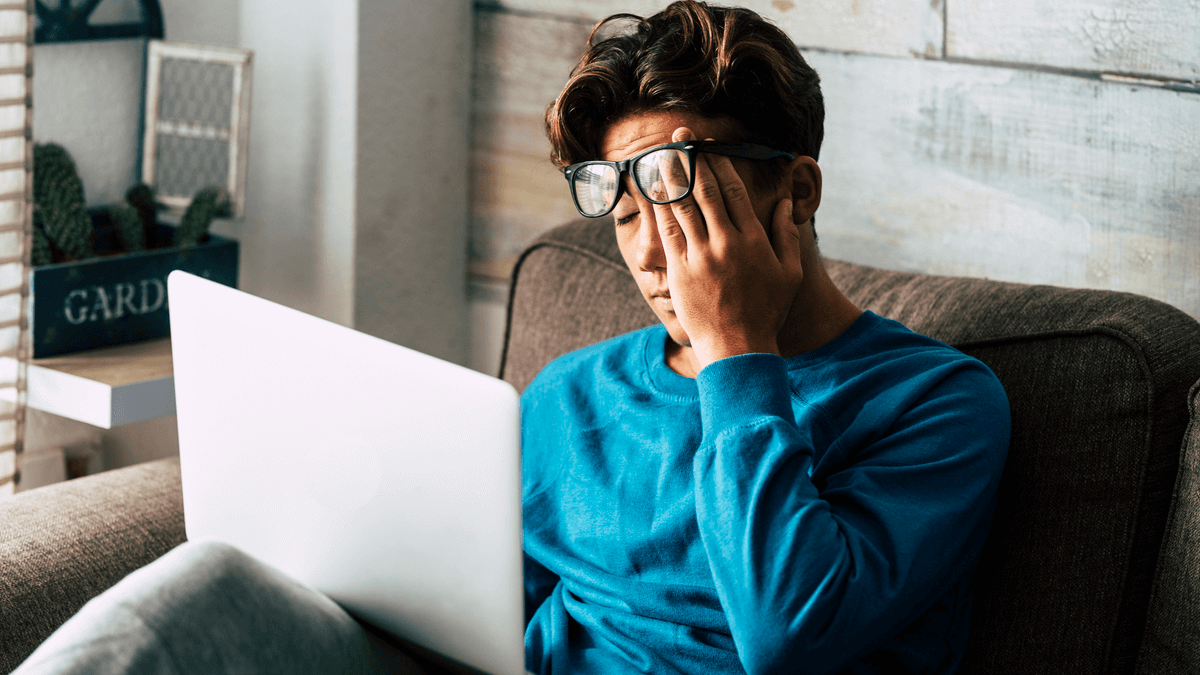 Jeune homme assis sur un canapé et affecté par ce qu'il voit sur les réseaux sociaux