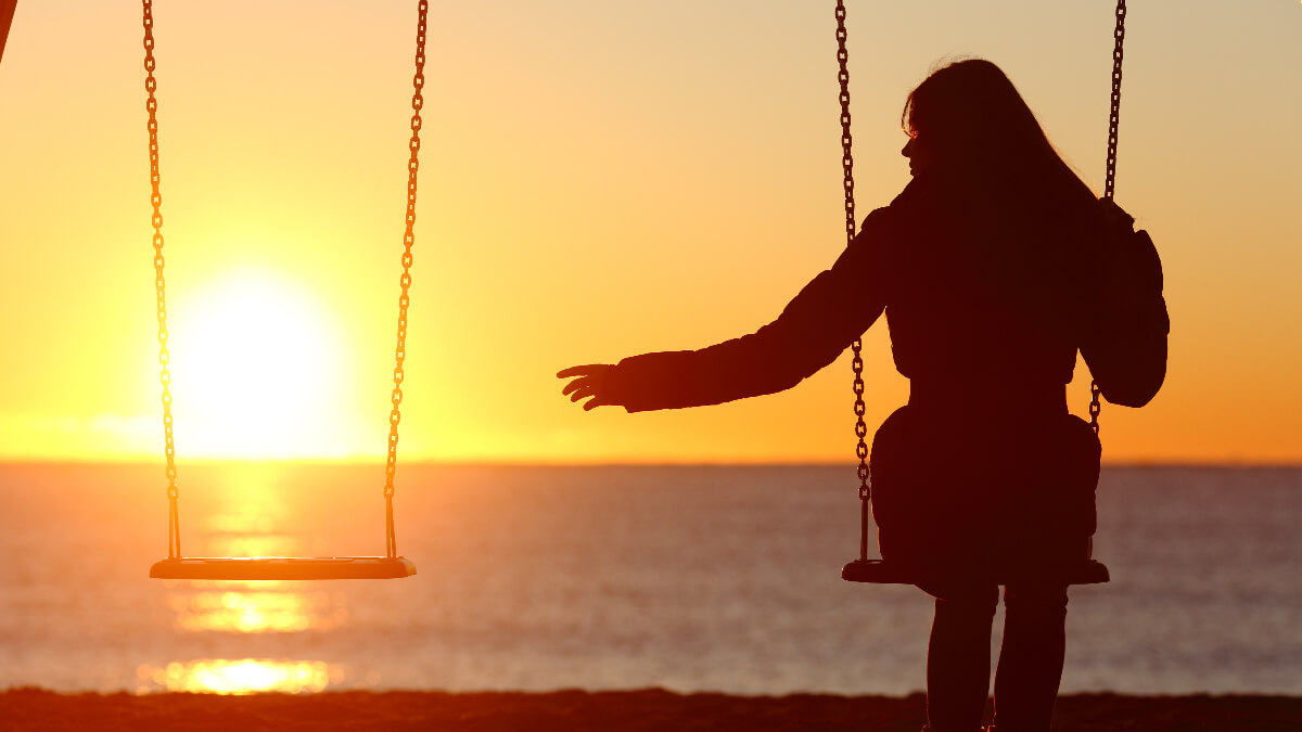 Mujer sentada en columpio con otro al lado vacío, por la pérdida de su pareja.
